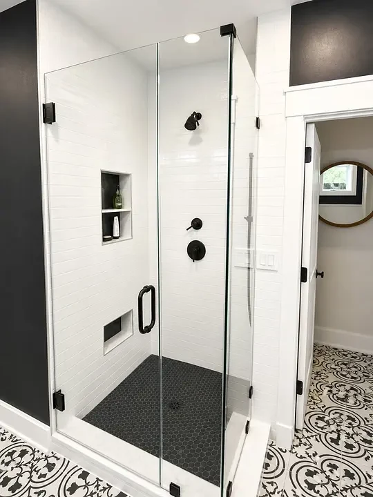 Glass shower enclosure with black hardware and white subway tile.
