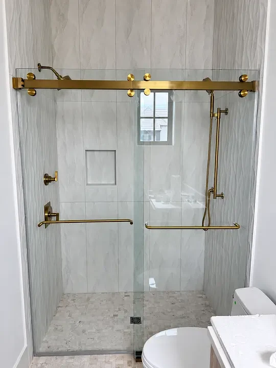 Modern shower with glass doors and gold fixtures, featuring a handheld showerhead and built-in wall niche.