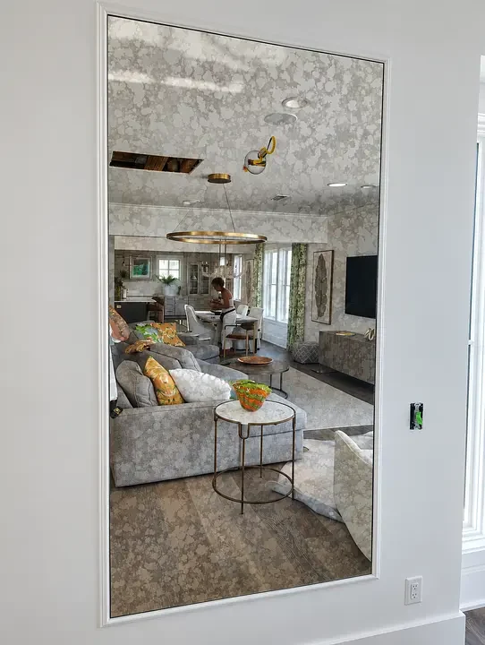 Reflective mirror showing a living room with a man standing near the kitchen island, surrounded by furniture and decor.