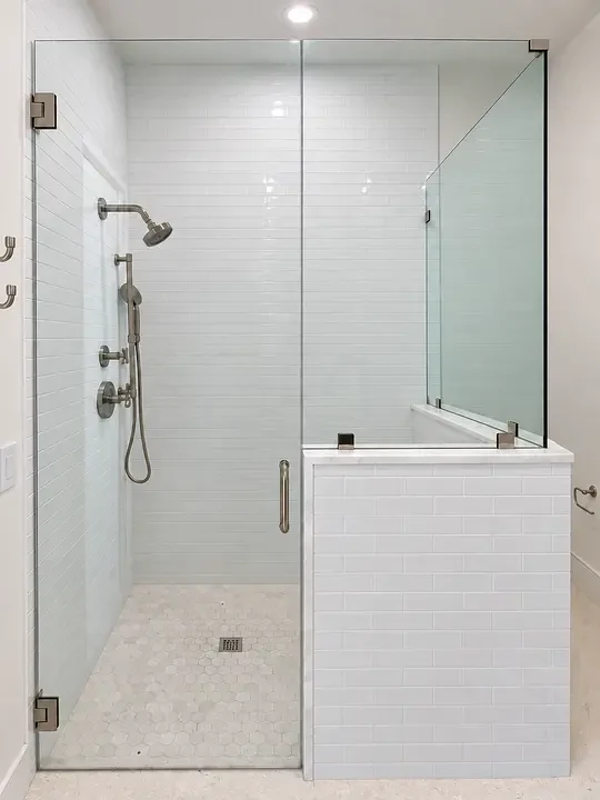 Modern shower with glass door, silver fixtures, white subway tiles, and hexagonal floor tiles.