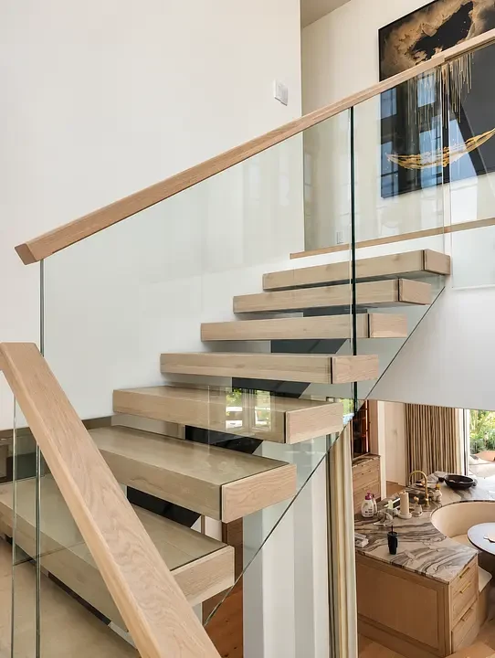 Modern wooden staircase with glass railing in a bright, open living space. Abstract art hangs on the wall.