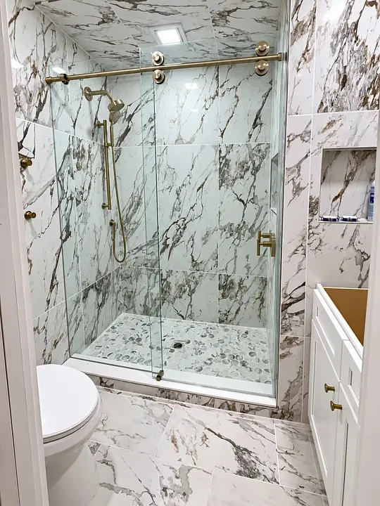Marble-tiled bathroom with glass shower, brass fixtures, and white cabinet.