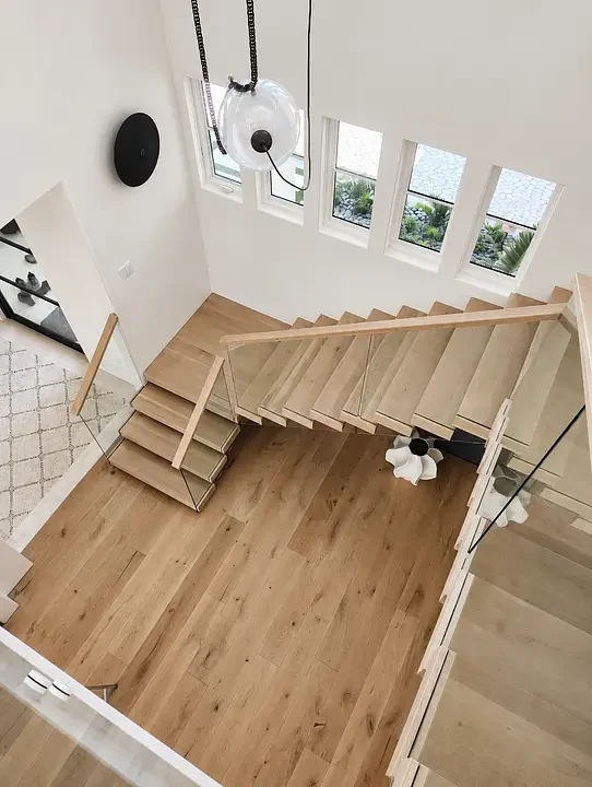 Modern staircase with wooden steps, glass railing, pendant light, and windows overlooking greenery.