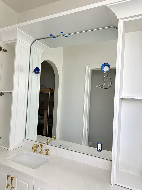 Bathroom under construction with white cabinets, a mirror, gold faucet, and exposed wiring for fixtures.
